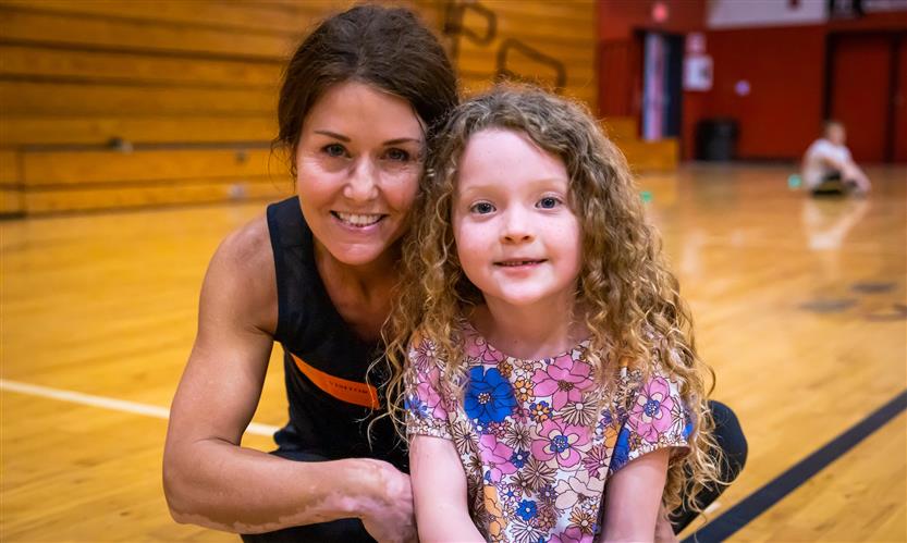 A mother and daughter smile while participating in a PE class